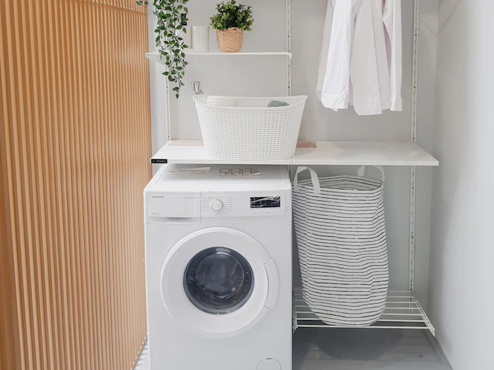 Bright home laundry area with a front-load washer below open shelves and a hanging rail
