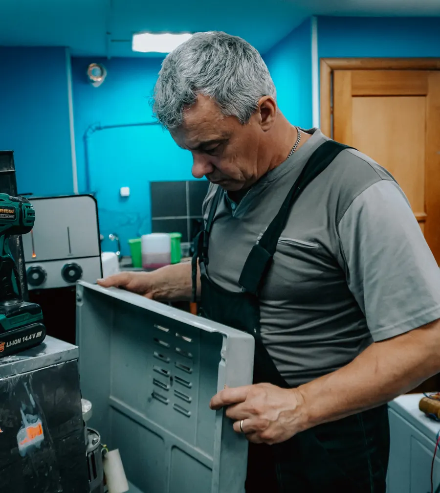 Appliance technician examining a removed appliance panel at a repair workbench
